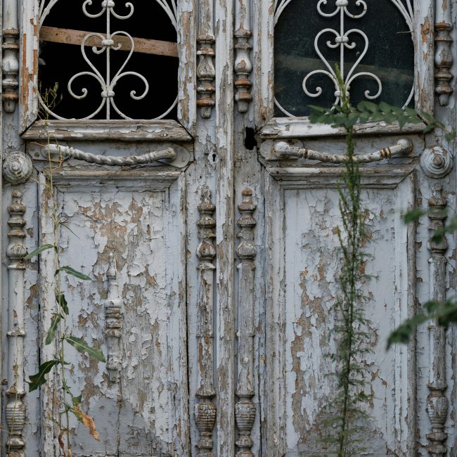 Close-up d'une porte en bois vieilli avec des ferrures décoratives, mettant en valeur son charme usé et ses détails rustiques.
