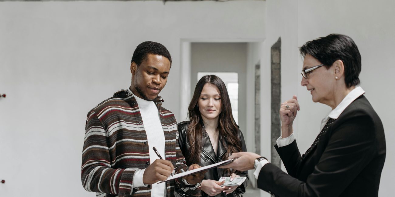 Un couple diversifié signant des documents avec un agent immobilier dans un nouveau cadre de maison.