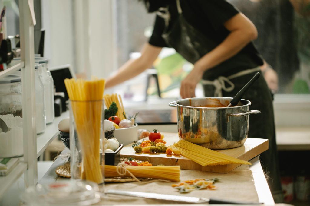 Côté vue d'une femme anonyme en tablier cuisinant des spaghettis dans une cuisine moderne et lumineuse.