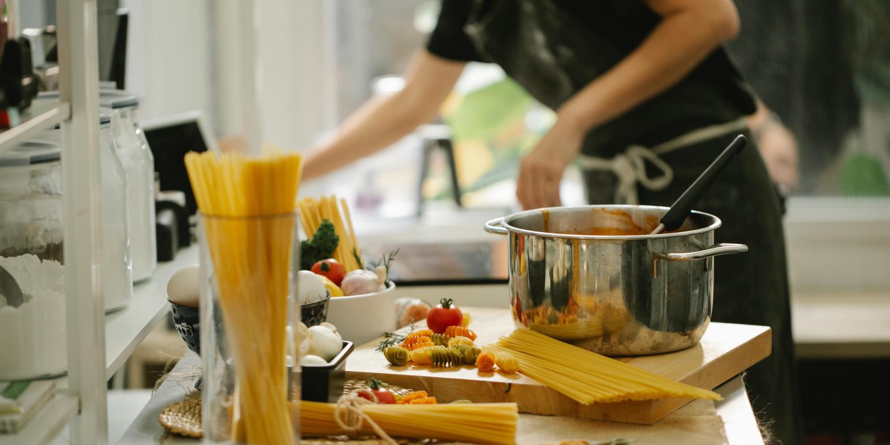 Côté vue d'une femme anonyme en tablier cuisinant des spaghettis dans une cuisine moderne et lumineuse.