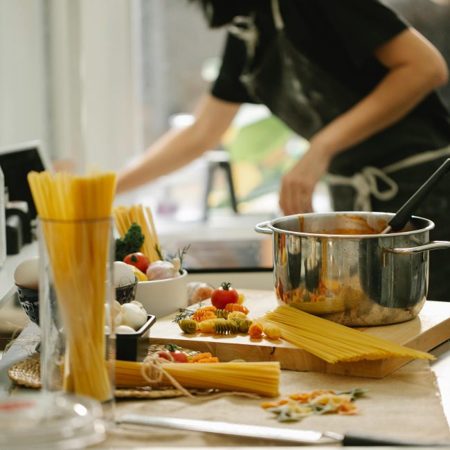 Côté vue d'une femme anonyme en tablier cuisinant des spaghettis dans une cuisine moderne et lumineuse.