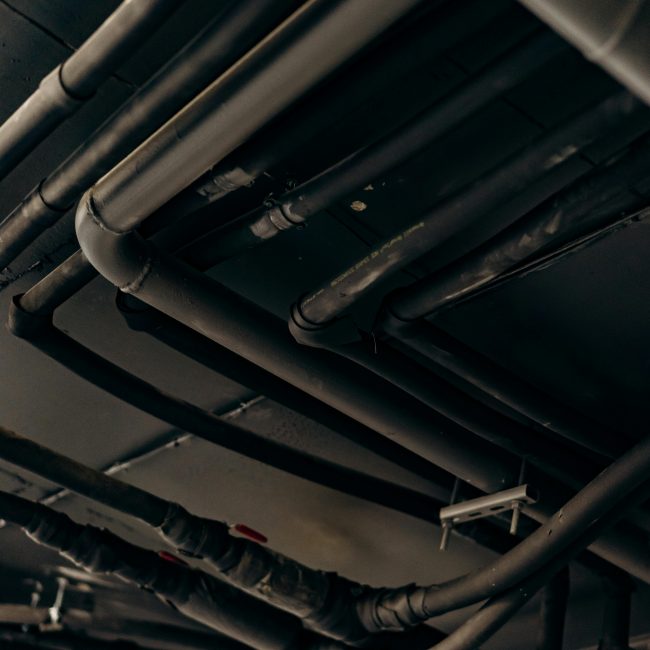 Un plan vertical de tuyaux et tubes en acier industriel dans un environnement faiblement éclairé.