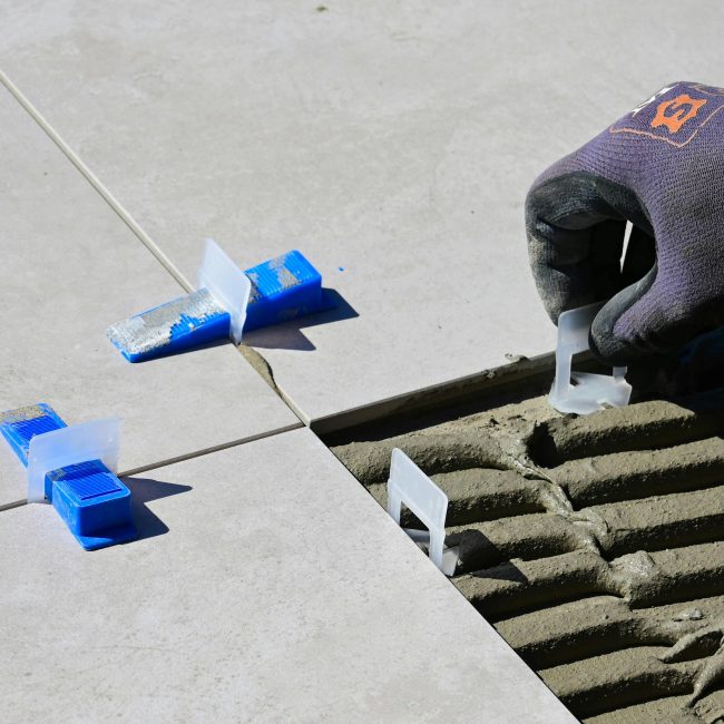 Close-up d'une installation professionnelle de carreaux utilisant des croisillons et des nivelleurs pour un alignement parfait.