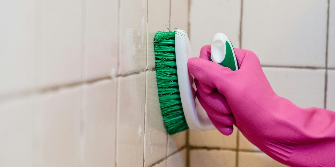Une personne nettoie des carreaux de salle de bain en portant un gant rose, mettant l'accent sur la propreté.