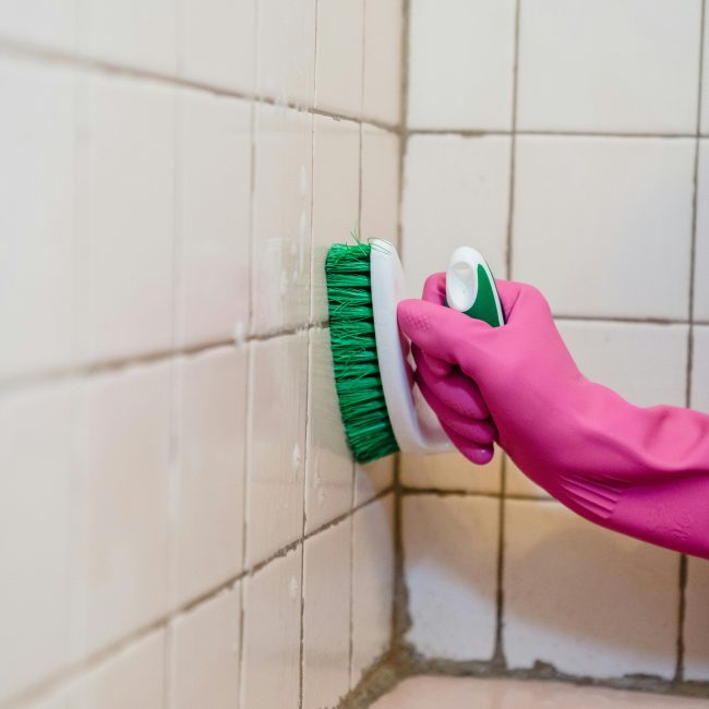 Une personne nettoie des carreaux de salle de bain en portant un gant rose, mettant l'accent sur la propreté.