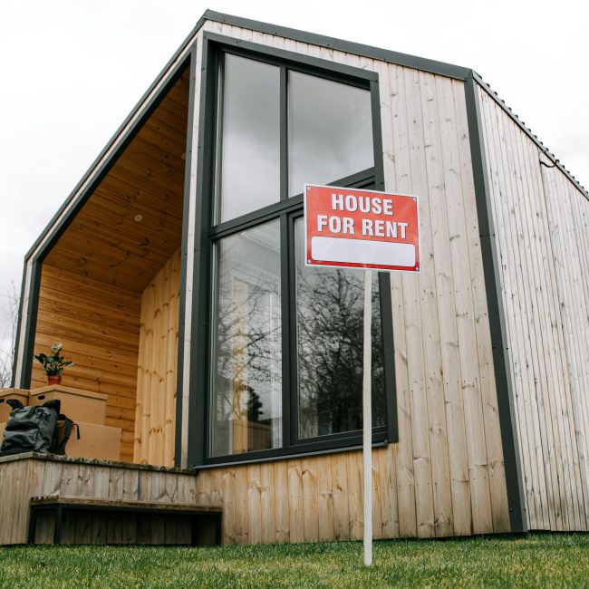 Vue en contre-plongée d'une maison moderne en bois avec une pancarte "Maison à louer", mettant en valeur une architecture contemporaine.