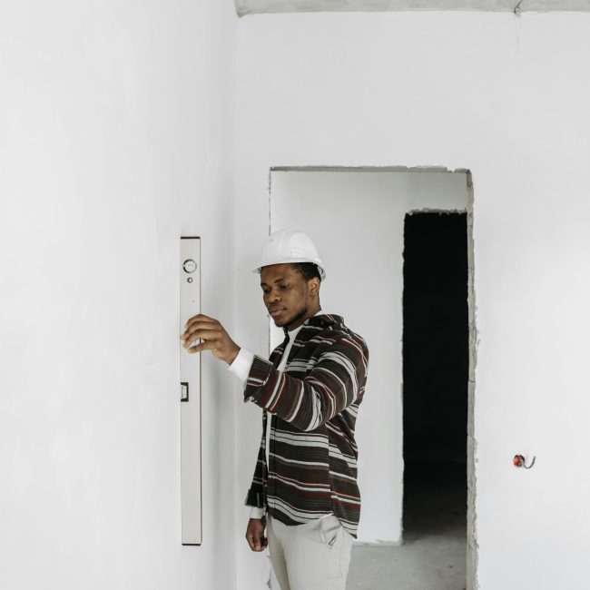 Architecte portant un casque de chantier vérifiant l'alignement d'un mur dans un projet de rénovation.