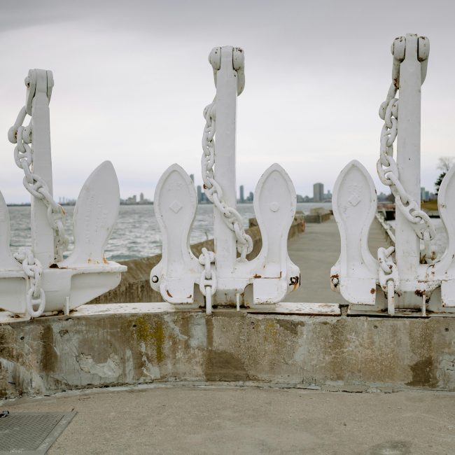 Rangée d'ancres blanches fixées sur un mur en béton en bord de mer. Ciel couvert et ligne d'horizon de la ville au loin.