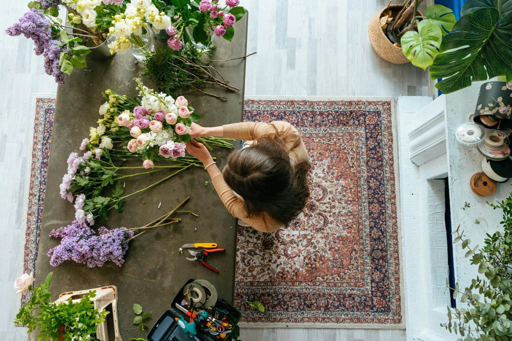 Vue de dessus d'un fleuriste arrangeant un bouquet sur une table en bois à l'intérieur. Affichage floral lumineux et coloré.
