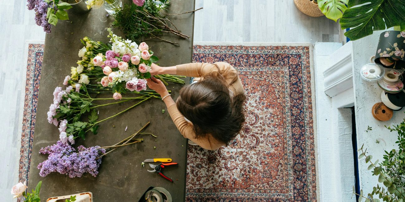 Vue de dessus d'un fleuriste arrangeant un bouquet sur une table en bois à l'intérieur. Affichage floral lumineux et coloré.