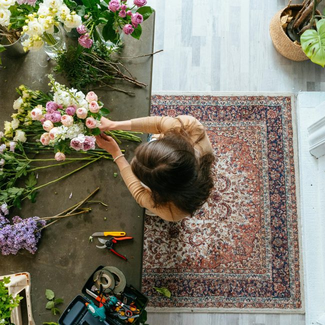 Vue de dessus d'un fleuriste arrangeant un bouquet sur une table en bois à l'intérieur. Affichage floral lumineux et coloré.