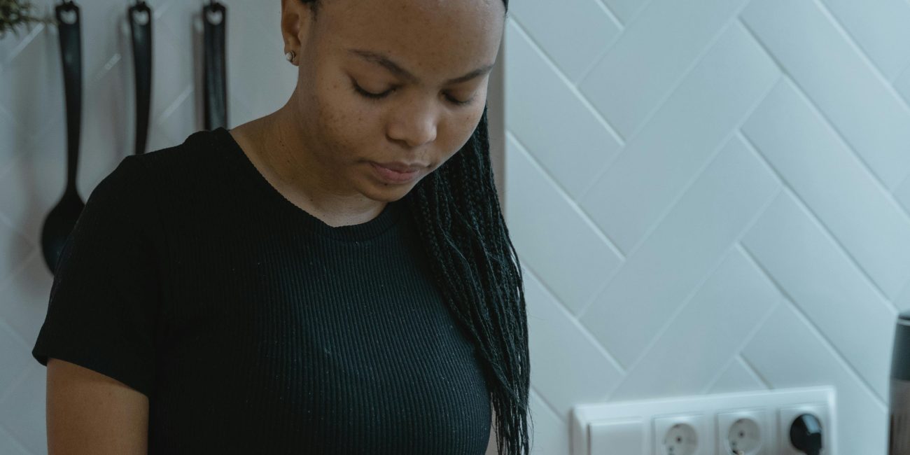 Une jeune femme dans une cuisine tenant un test de grossesse, plongée dans ses pensées.