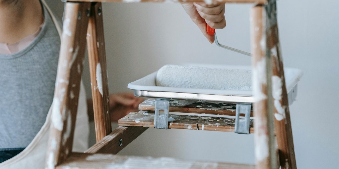 Femme adulte utilisant un rouleau et une échelle pour peindre un mur de pièce en intérieur.