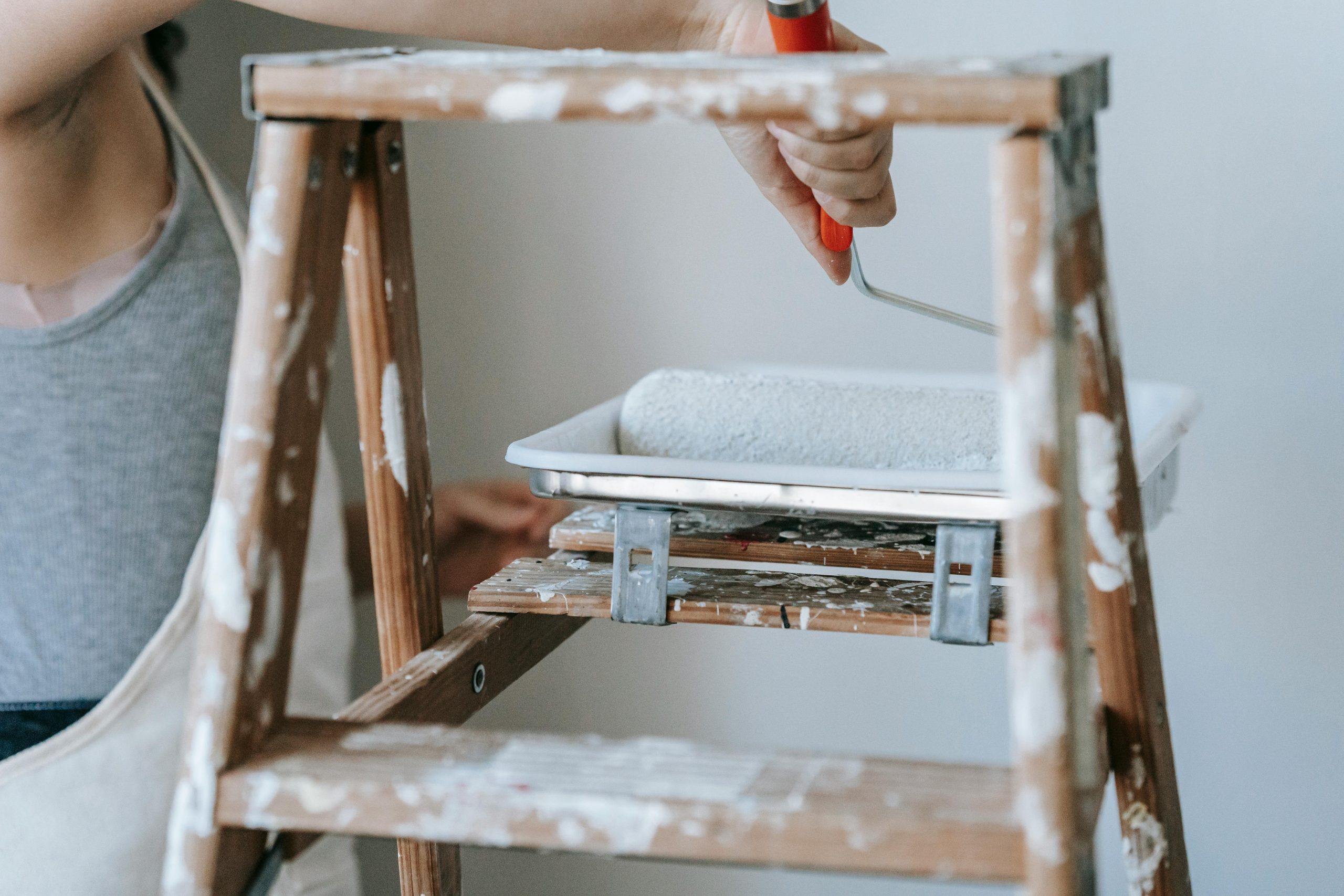 Femme adulte utilisant un rouleau et une échelle pour peindre un mur de pièce en intérieur.