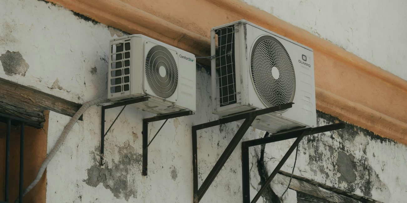 Two outdoor AC units installed on a weathered concrete wall for cooling purposes. Deux unités de climatisation extérieures installées sur un mur en béton usé à des fins de refroidissement.