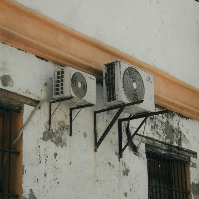 Two outdoor AC units installed on a weathered concrete wall for cooling purposes. Deux unités de climatisation extérieures installées sur un mur en béton usé à des fins de refroidissement.