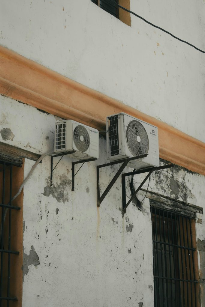 Two outdoor AC units installed on a weathered concrete wall for cooling purposes. Deux unités de climatisation extérieures installées sur un mur en béton usé à des fins de refroidissement.