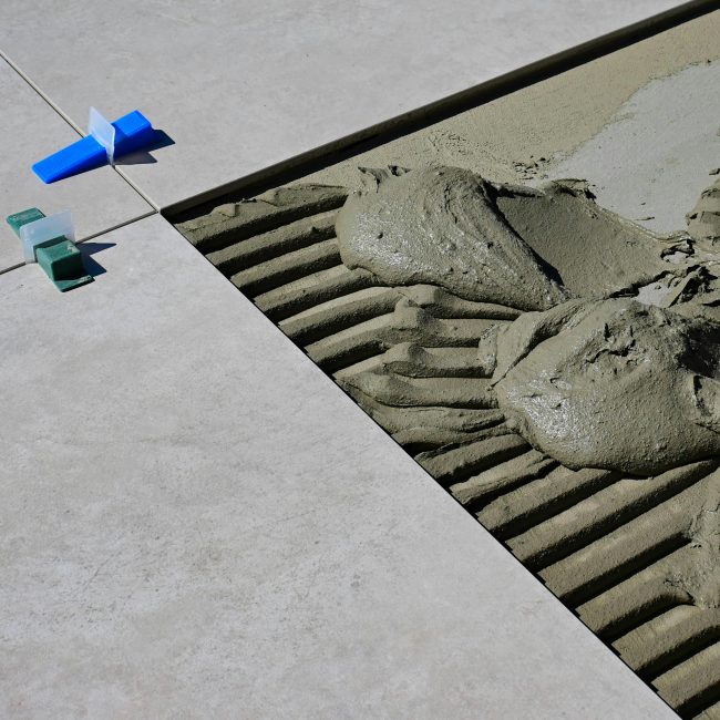 Gros plan de ciment humide et de croisillons lors de la pose de carrelage au sol.