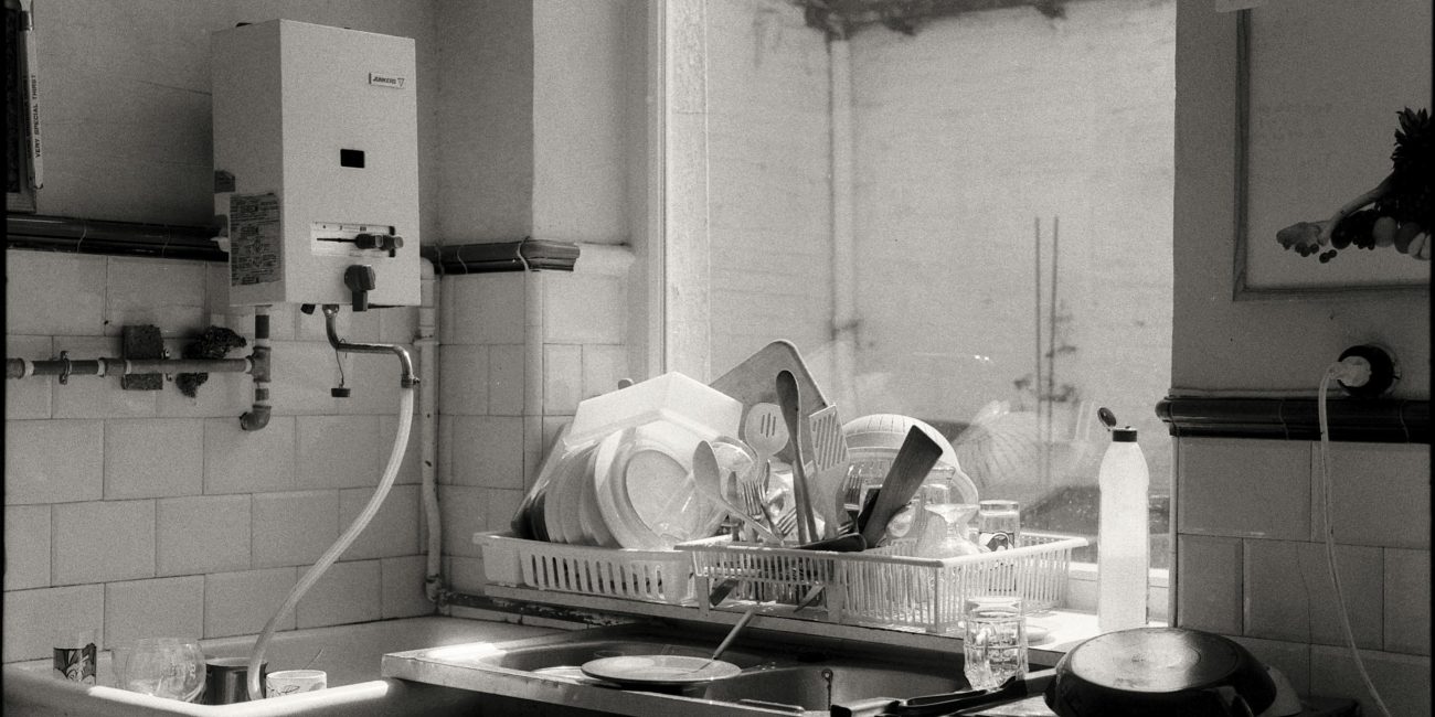 Image en noir et blanc d'un évier de cuisine rempli de vaisselle et de couverts près de la fenêtre.