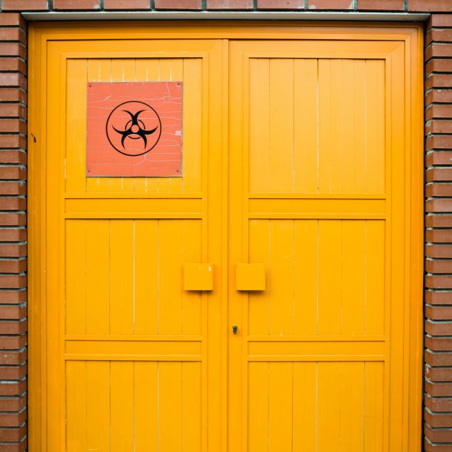 Porte jaune vif avec un symbole de danger biologique apposé sur un mur de briques rouges, symbolisant la prudence et le danger.