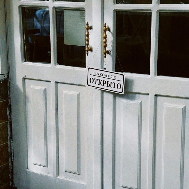 Porte blanche traditionnelle à double battant avec un panneau "Открыто" (Ouvert) en russe, entrée accueillante.