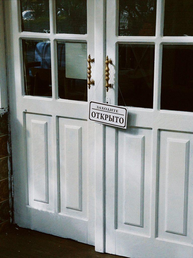 Porte blanche traditionnelle à double battant avec un panneau "Открыто" (Ouvert) en russe, entrée accueillante.