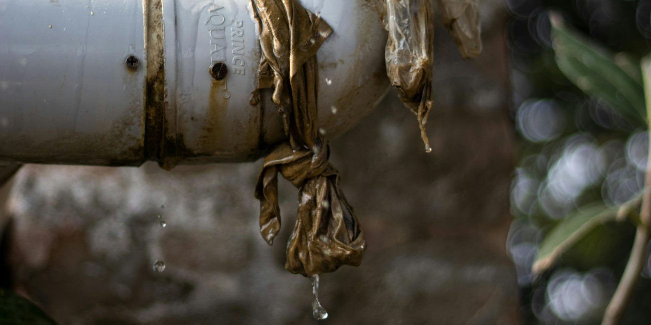 Gros plan d'un tuyau en plastique qui fuit à l'extérieur avec de l'eau qui goutte, montrant des signes d'usure.