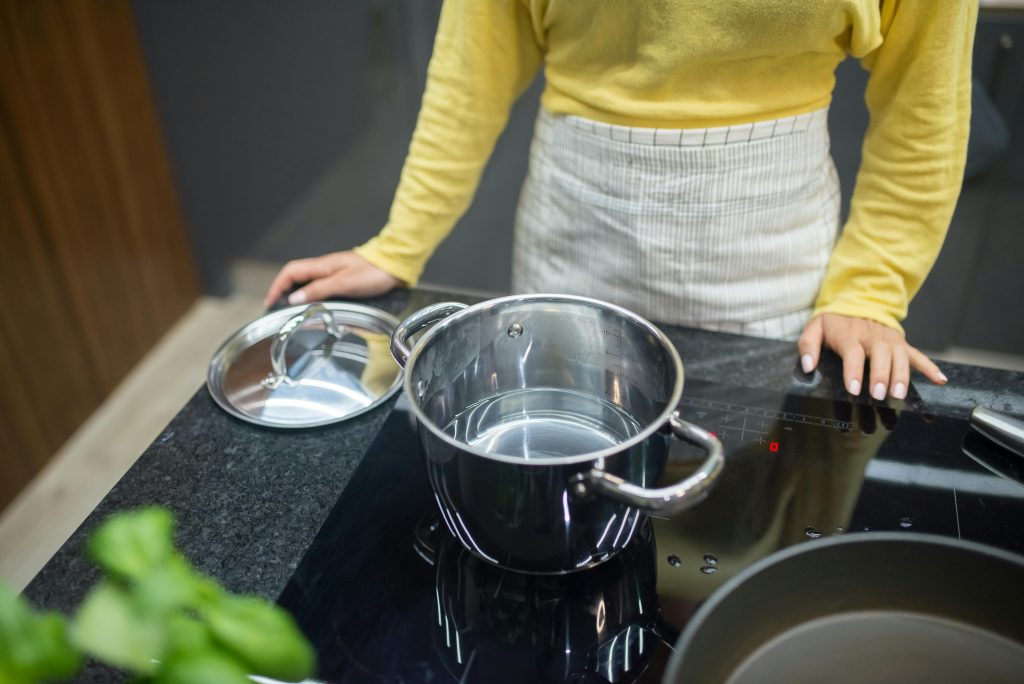 Une femme en pull jaune cuisinant sur une plaque à induction avec une casserole en inox.