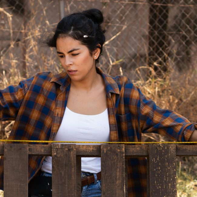 Focused woman using measuring tape on fence, showcasing empowerment in carpentry. Femme concentrée utilisant un mètre ruban sur une clôture, illustrant l'autonomisation en menuiserie.