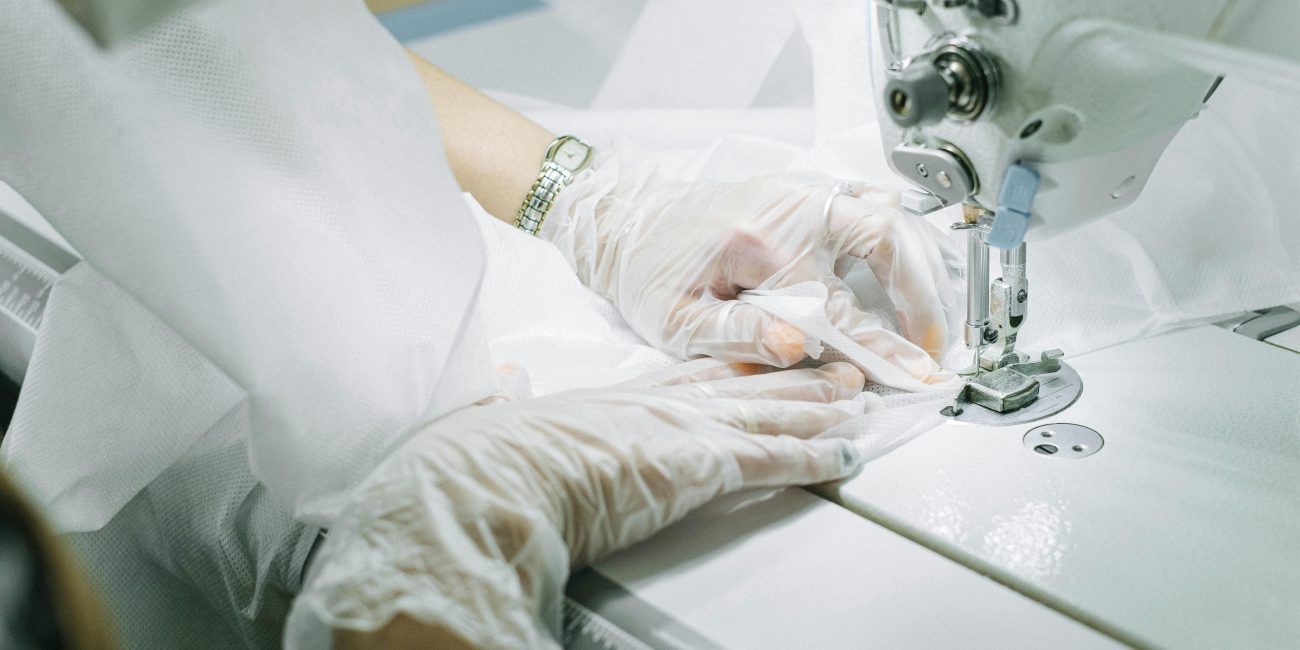 Mains gantées travaillant sur une machine à coudre, créant un vêtement.