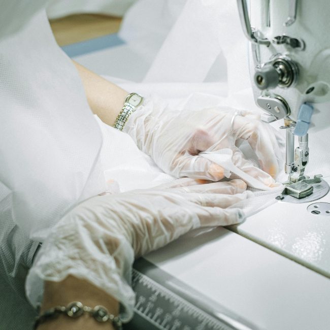 Mains gantées travaillant sur une machine à coudre, créant un vêtement.