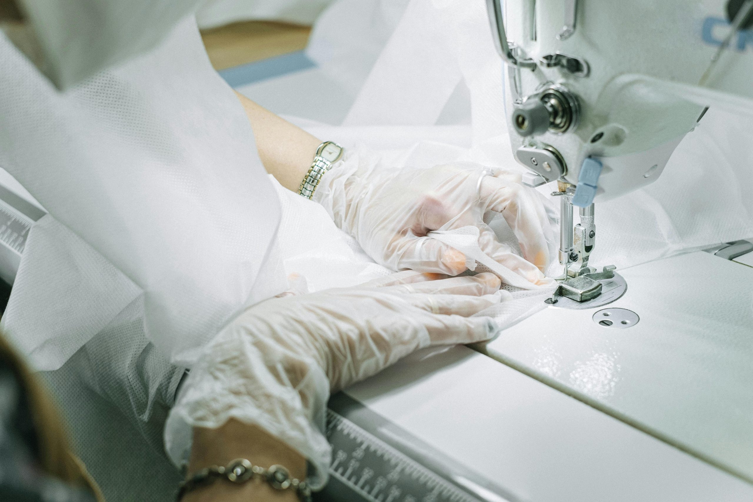Mains gantées travaillant sur une machine à coudre, créant un vêtement.