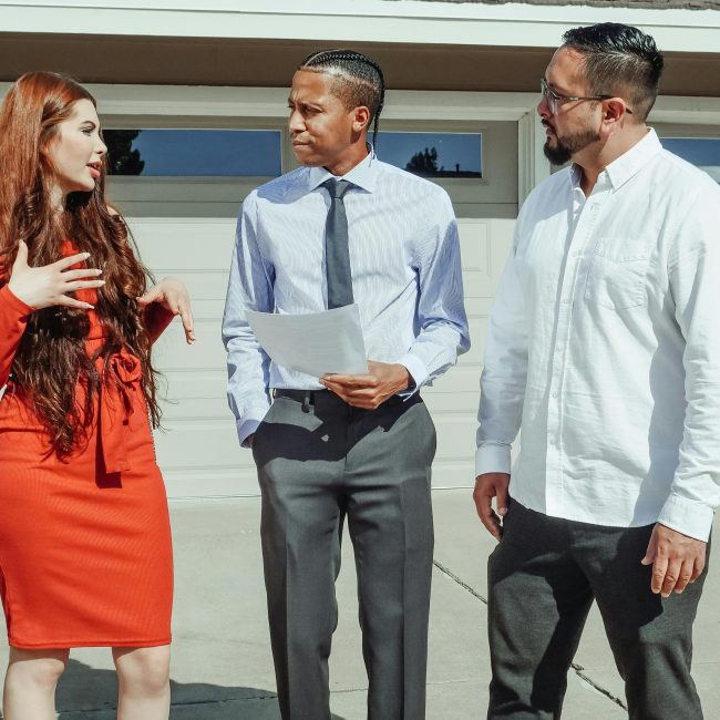 Un jeune couple discutant avec un agent immobilier devant une maison moderne.