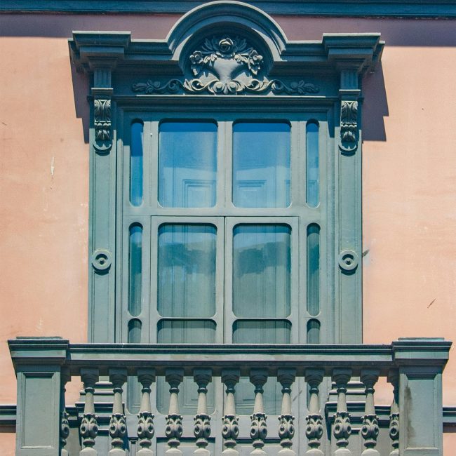 Close-up d'un balcon ensoleillé orné avec des détails architecturaux classiques sur un mur urbain.