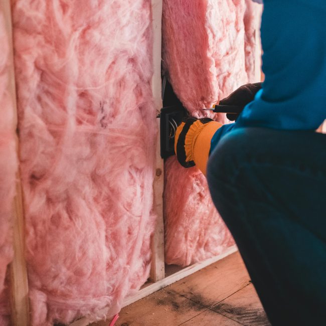 Focused worker installant de l'isolation en fibre de verre rose à l'intérieur d'un bâtiment.
