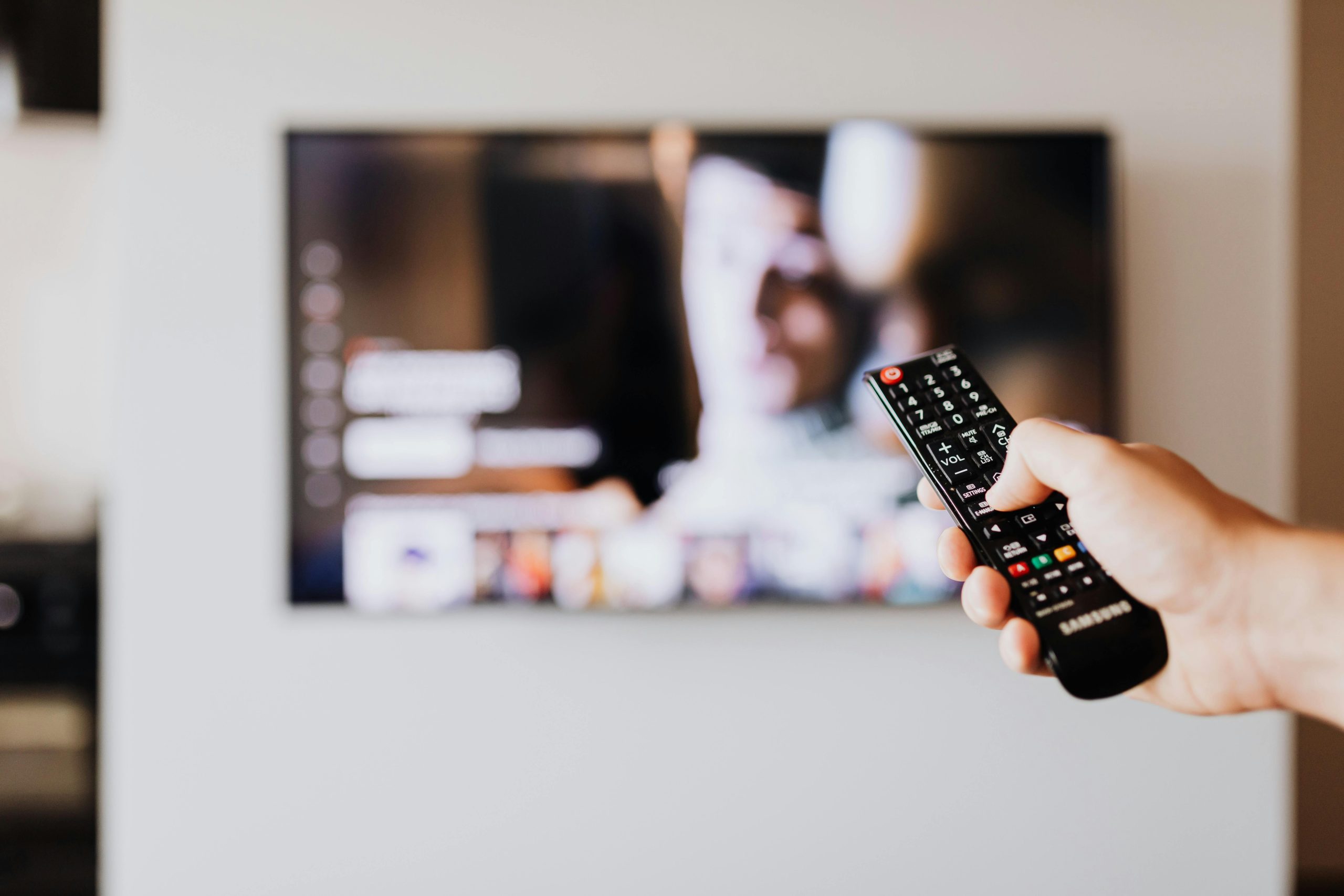 Person utilisant une télécommande avec un écran de télévision flou en arrière-plan.