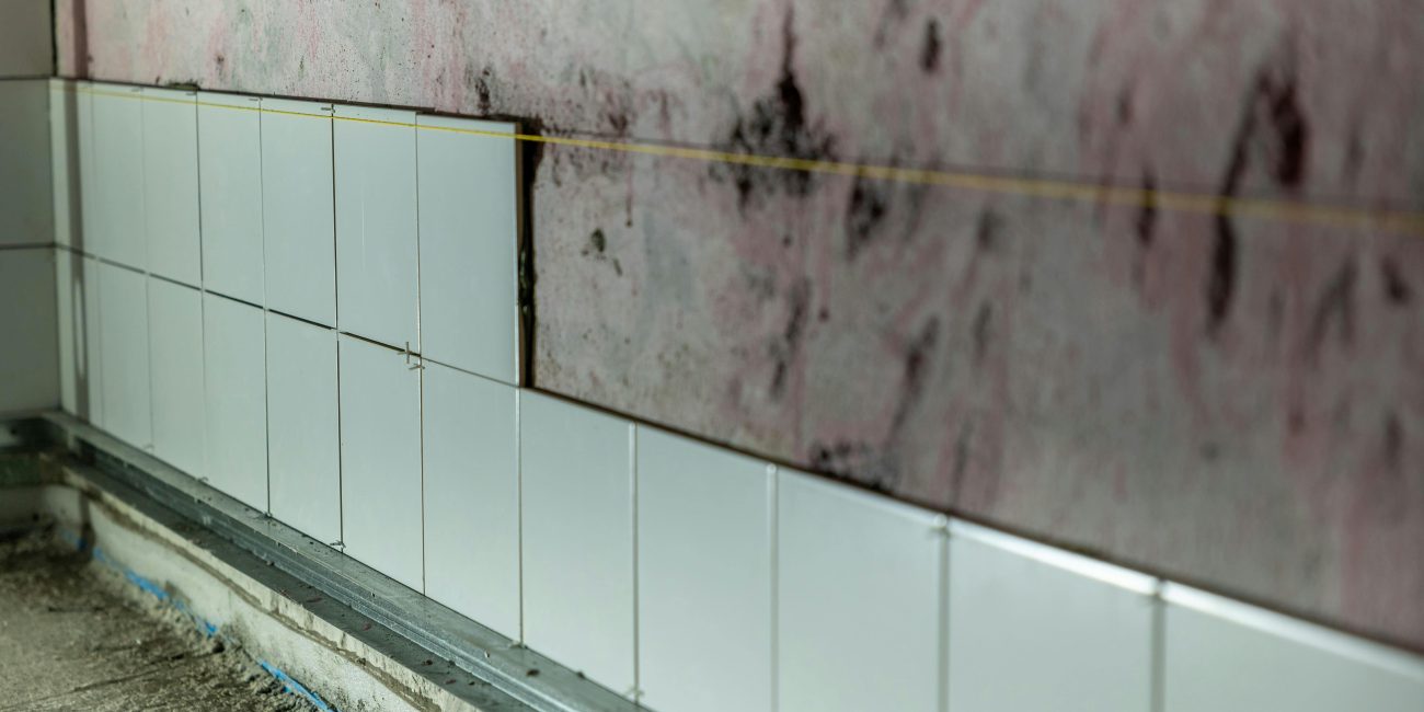 Close-up d'un mur partiellement carrelé dans une zone de construction, montrant des travaux de rénovation inachevés.