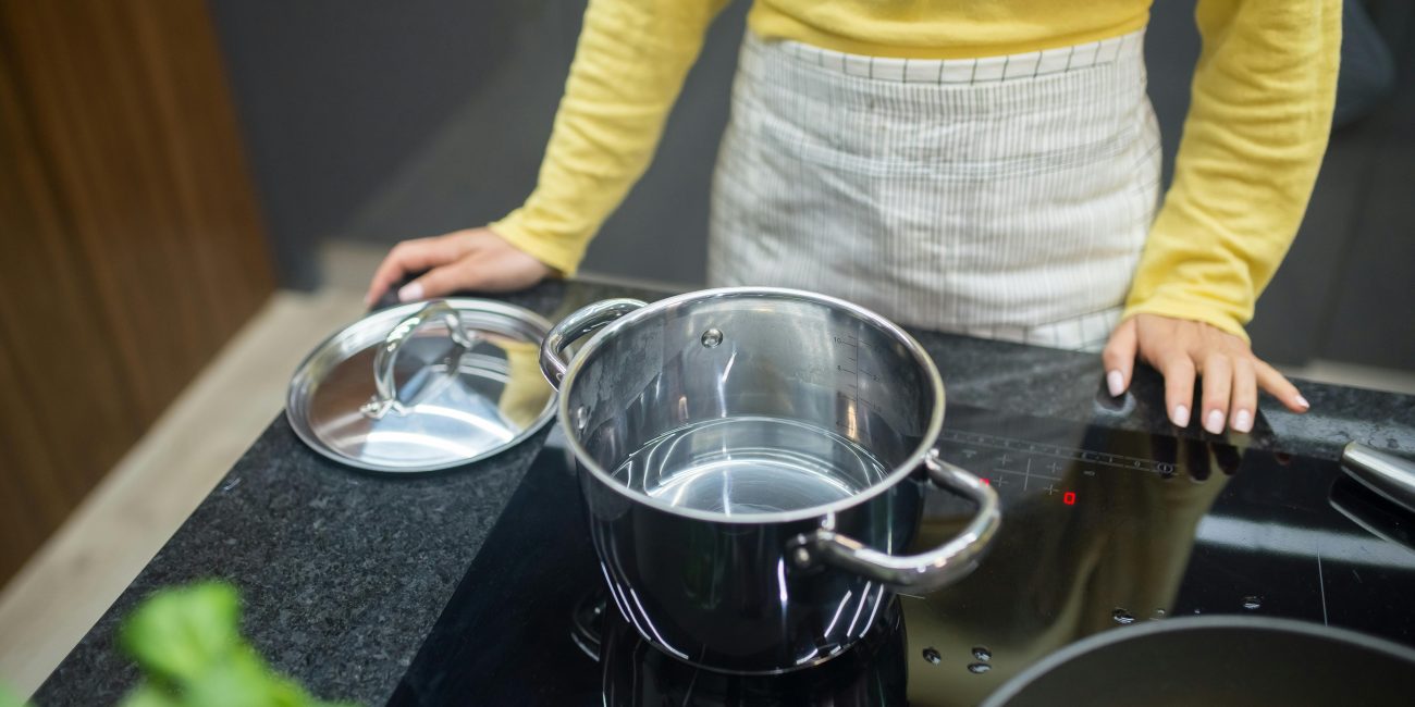 Une femme en pull jaune cuisinant sur une plaque à induction avec une casserole en inox.