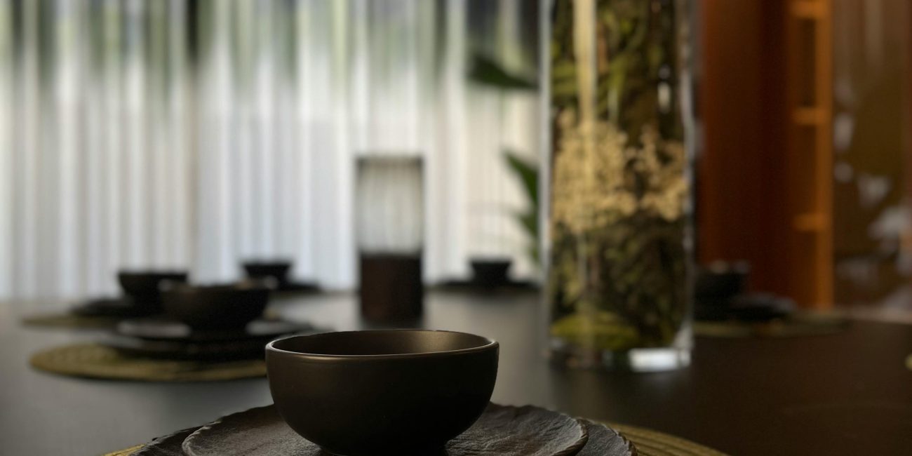 Stylish dining setup avec des assiettes noires et des couverts dorés sur un set de table tissé, éclairage doux