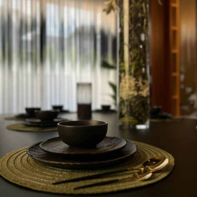 Stylish dining setup avec des assiettes noires et des couverts dorés sur un set de table tissé, éclairage doux