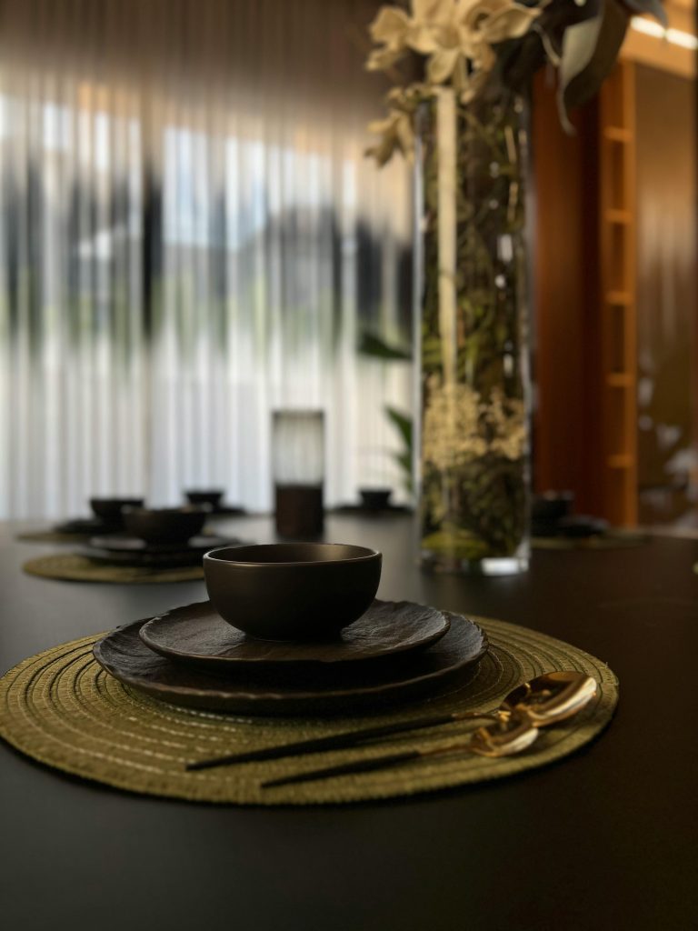 Stylish dining setup avec des assiettes noires et des couverts dorés sur un set de table tissé, éclairage doux