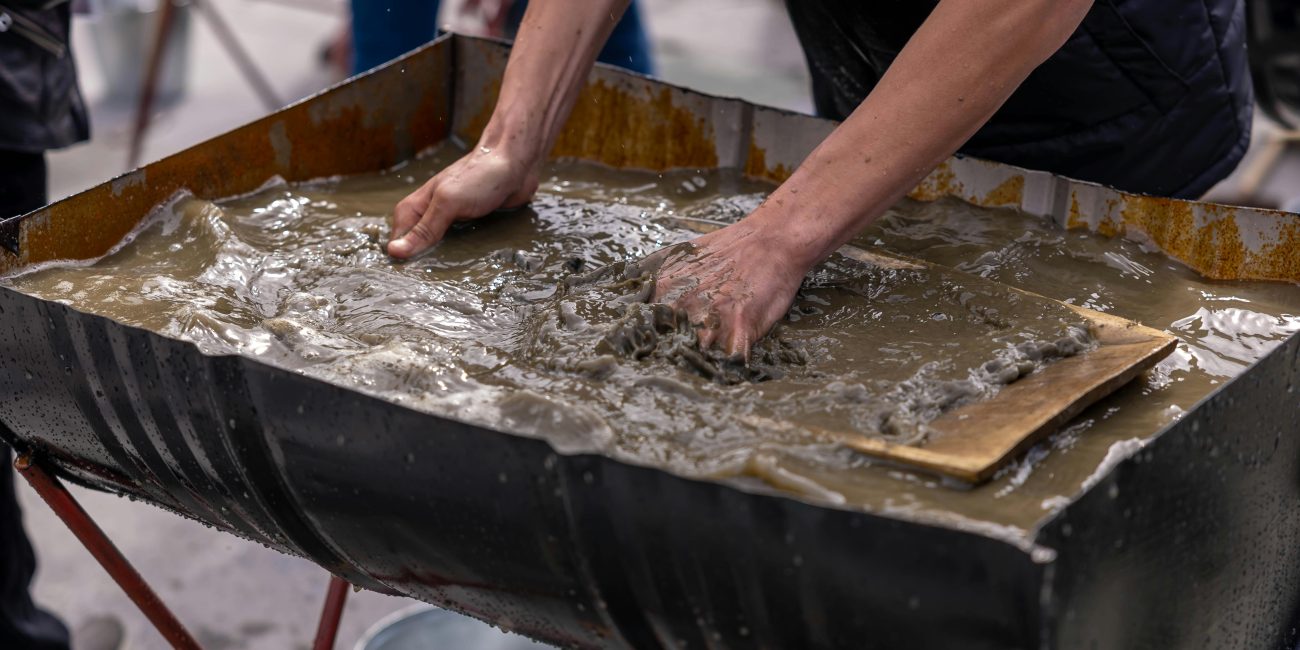 Mains mélangeant une boue de béton dans un grand conteneur pour des travaux de construction en extérieur.