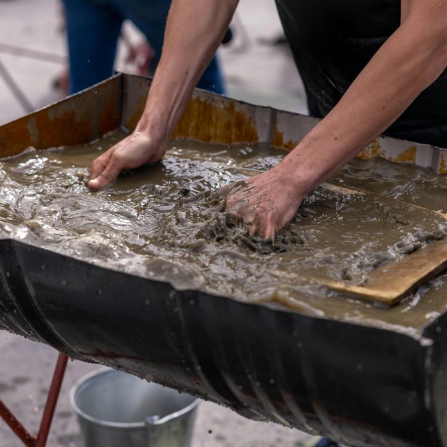 Mains mélangeant une boue de béton dans un grand conteneur pour des travaux de construction en extérieur.