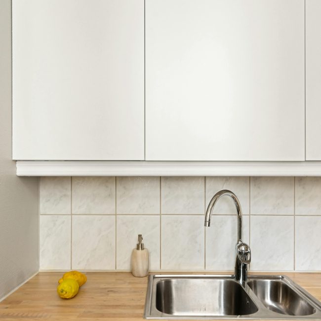 Cuisine minimaliste élégante avec évier en acier inoxydable, citron et armoires blanches.