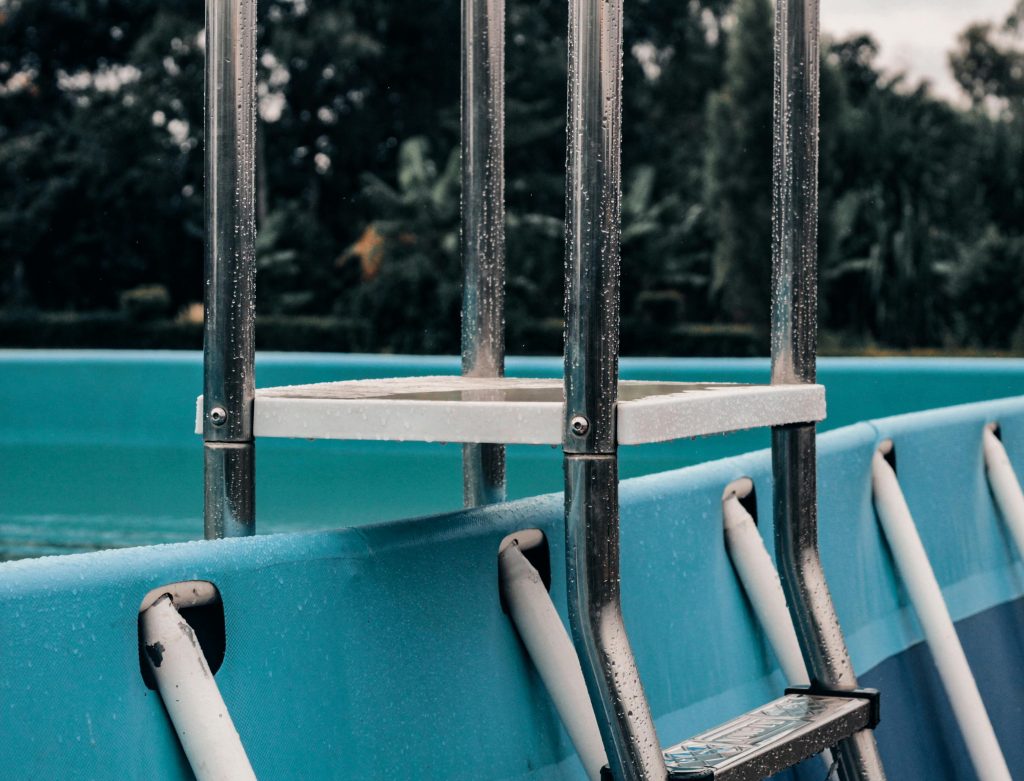 Une vue détaillée d'une échelle métallique fixée à une piscine extérieure, montrant des gouttelettes et un arrière-plan naturel serein.