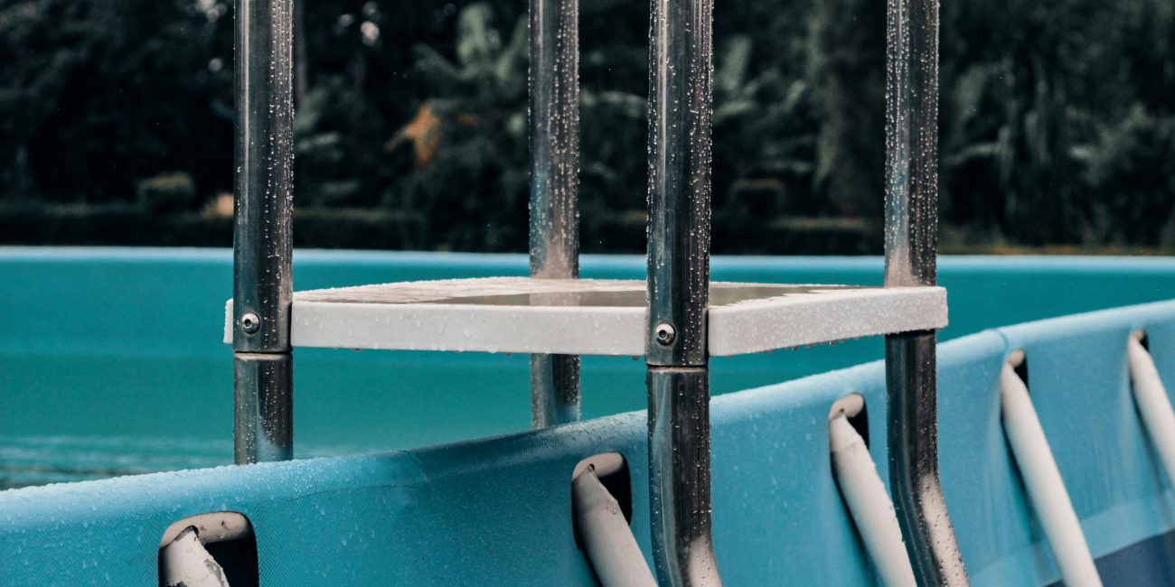 Une vue détaillée d'une échelle métallique fixée à une piscine extérieure, montrant des gouttelettes et un arrière-plan naturel serein.