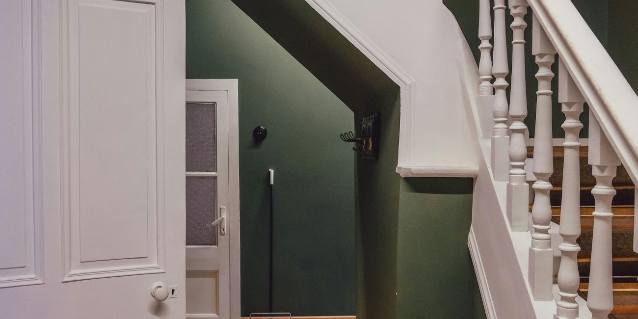 Un escalier en bois avec une rampe blanche contre des murs verts dans un intérieur chaleureux et cosy.