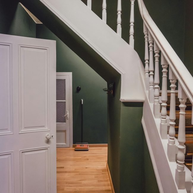 Un escalier en bois avec une rampe blanche contre des murs verts dans un intérieur chaleureux et cosy.