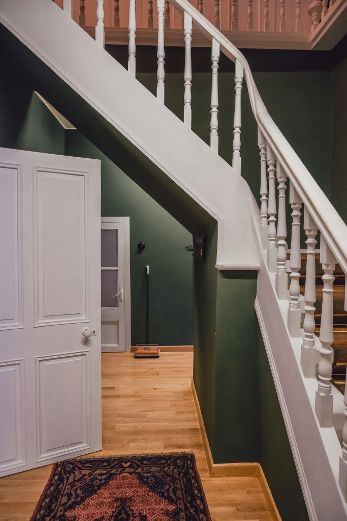Un escalier en bois avec une rampe blanche contre des murs verts dans un intérieur chaleureux et cosy.