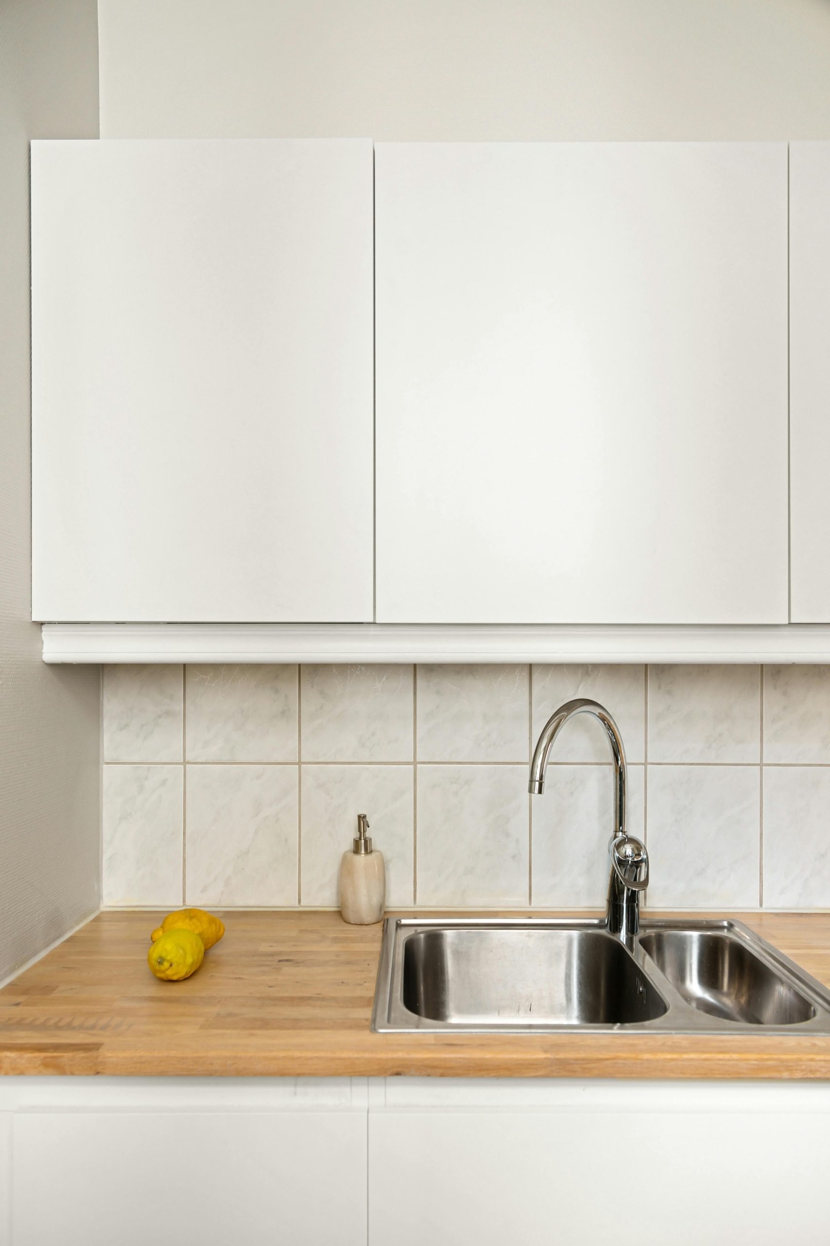 Élégante cuisine minimaliste avec évier en acier inoxydable, citron et placards blancs.